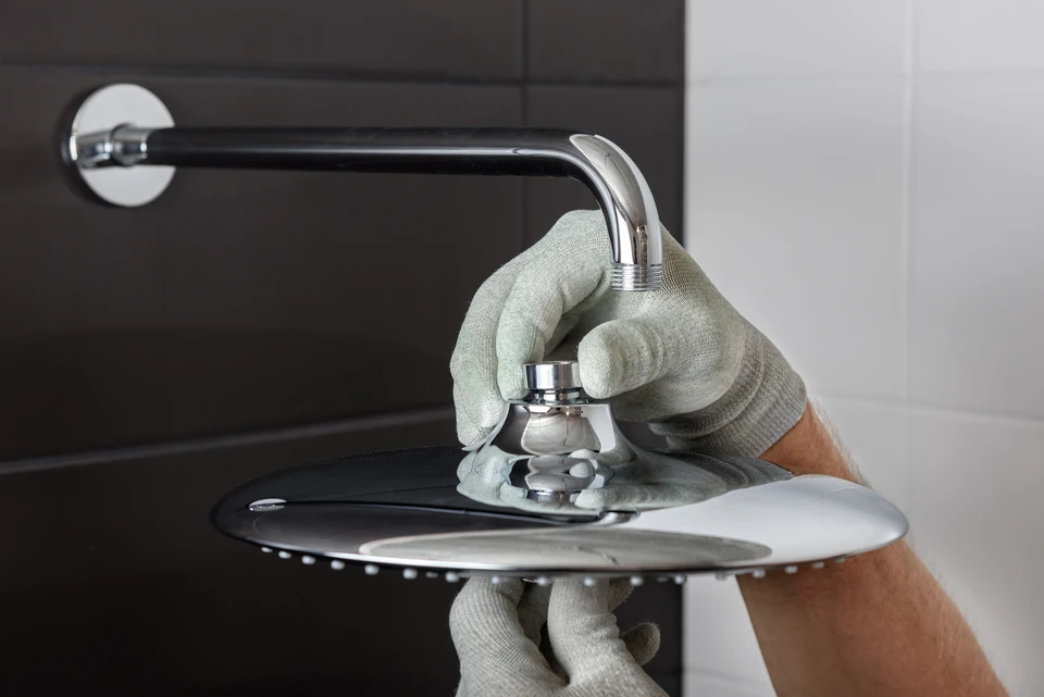 Plombier professionnel en combinaison de travail installant un robinet mural dans salle de bain carrelée blanche