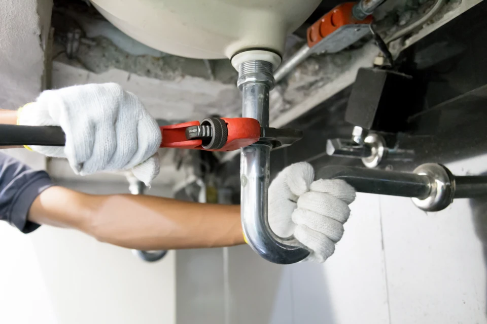 Un plombier en veste rouge utilise un chalumeau à gaz pour souder une canalisation en cuivre dans un environnement intérieur