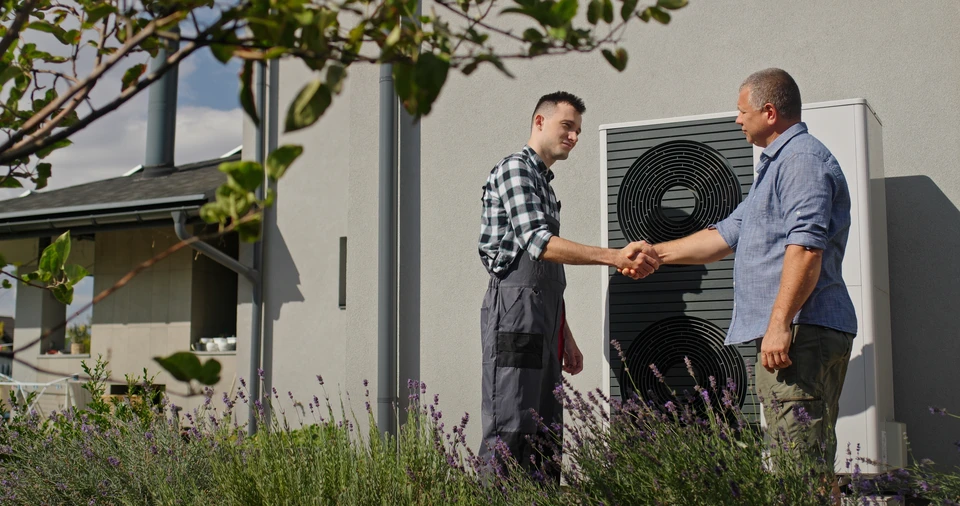Un technicien discute de l'entretien de la pompe à chaleur avec les propriétaires dans un jardin, près de l'unité externe